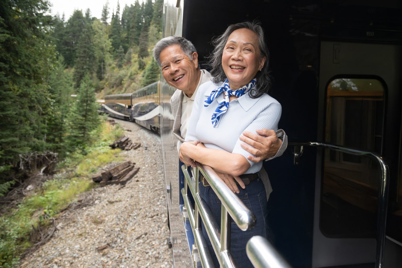 A host serving guests on the GoldLeaf outdoor viewing platform as the train runs through the mountains.