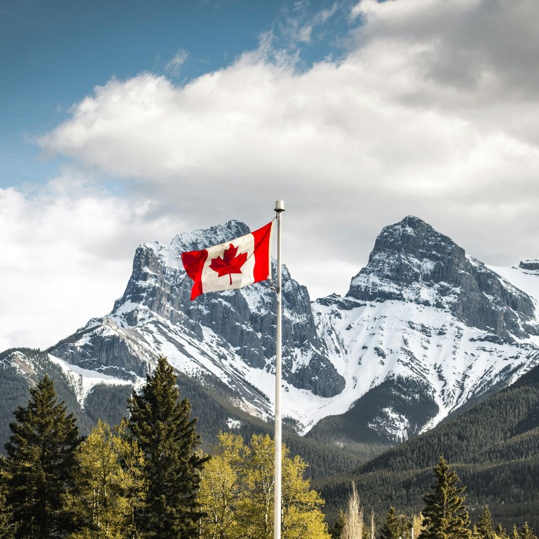 A Canadian flag flying against snow-covered Rocky Mountain peaks.